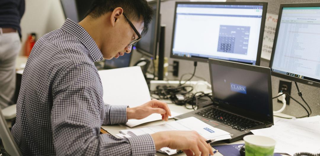 A Clark employee reads in front of computer screens at a desk in a Clark office