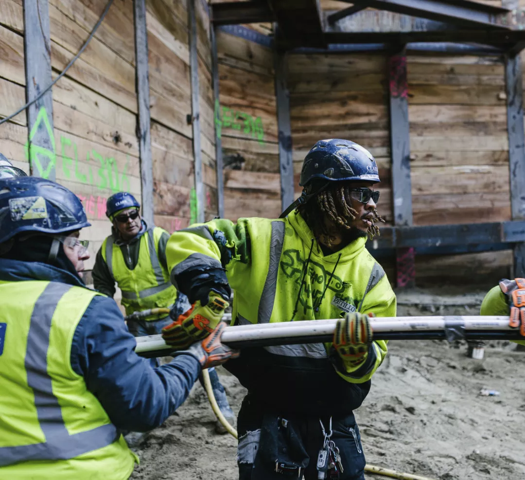 Clark Construction skilled craft team members work together in the foundation of a jobsite wearing neon PPE and blue safety helmets